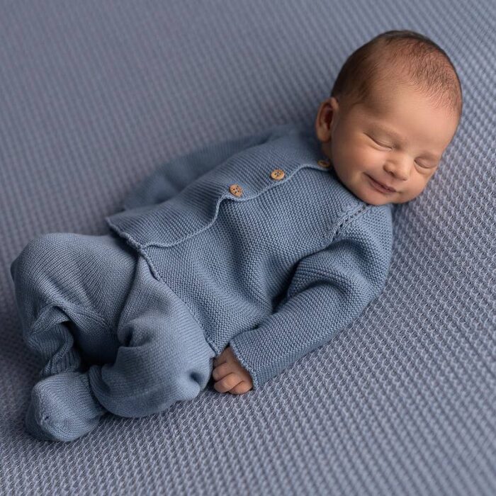 Un bebé recién nacido dormido con un mono de punto azul descansa pacíficamente sobre una manta con textura azul a juego