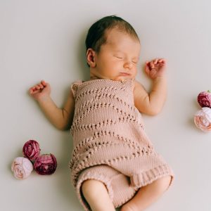 Un recién nacido dormido lleva el Mono rosa con forma de ondas rosa de micu micu sobre una superficie blanca