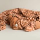 Pack recién nacidos camuflaje rojo ladrillo. Un bebé dormido está envuelto en una acogedora manta con estampado de ladrillo rojo camuflaje y lleva un gorro y un conjunto a juego de micu micu. El fondo neutro realza la atmósfera serena. Descubre productos para bebés con entrega gratis en Mallorca para completar los elementos esenciales de la habitación del bebé sin esfuerzo.