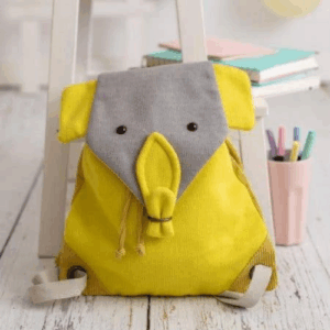 Crochetts - MOCHILA KOALA Sobre un suelo de madera blanca se encuentra la mochila Crochetts - MOCHILA KOALA, una mochila amarilla con una solapa gris con motivos de elefantes. Cerca, un taburete blanco sostiene libros y lápices, ideal para coger chupetes para bebés baratos o echar un vistazo a los productos para bebés con entrega gratis en Mallorca.