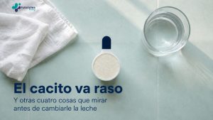 Cacito dosificador de leche infantil enrasado, junto a un vaso de agua sobre una encimera clara